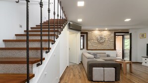 A modern interior with a wooden staircase, a stone accent wall, and a cozy seating area with a sofa and ottoman. - Villa Stonehouse (Istria - Umag) (Umag)