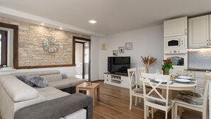 A modern living room with a stone accent wall, a large sofa, a dining area with a round table, and a kitchen with white cabinets. - Villa Stonehouse (Istria - Umag) (Umag)