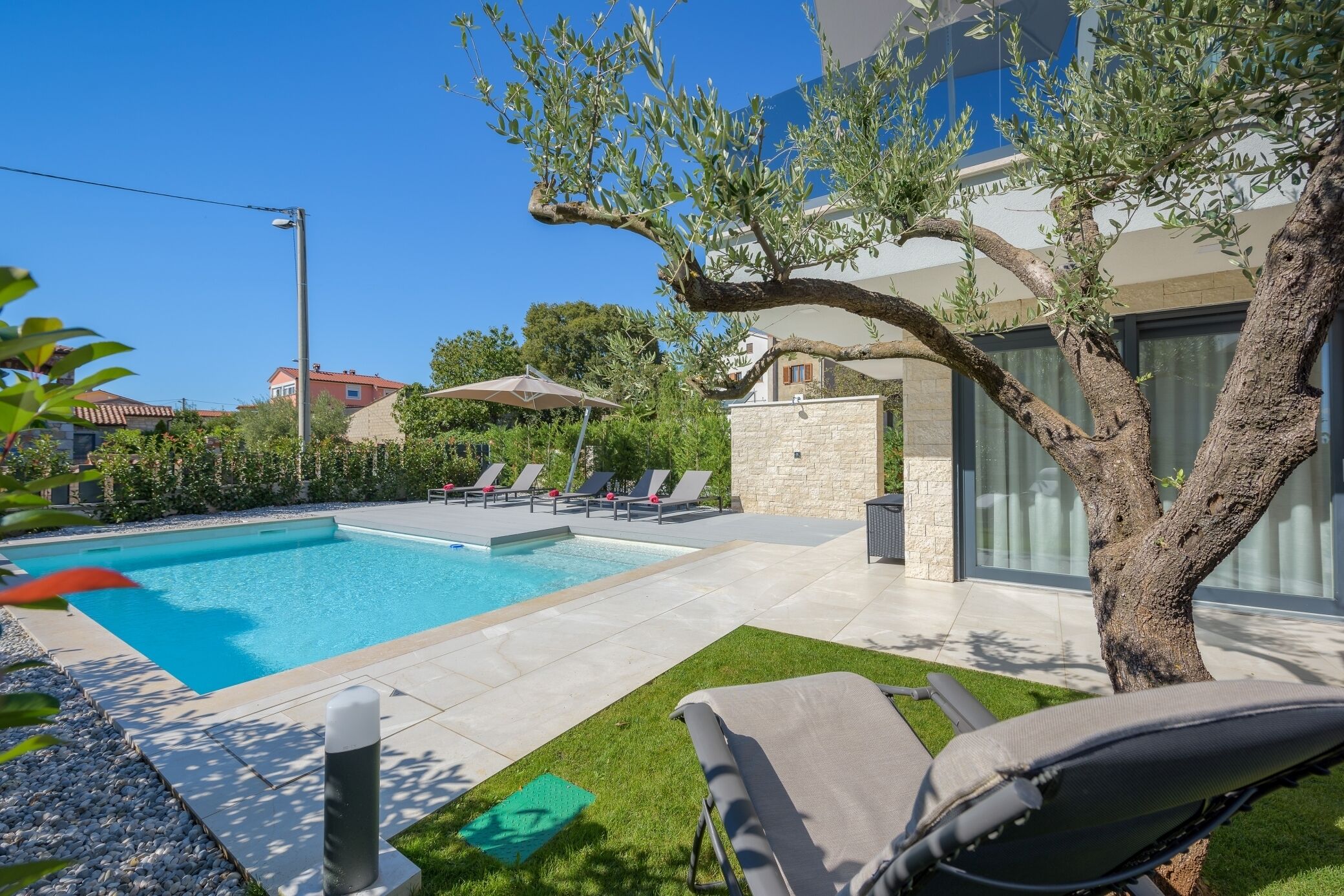 A swimming pool with lounge chairs and umbrellas, surrounded by a stone wall and greenery.