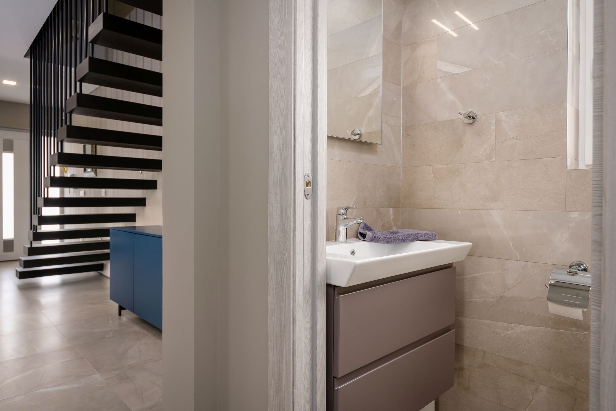 A modern bathroom with a sink, mirror, and towel rack.