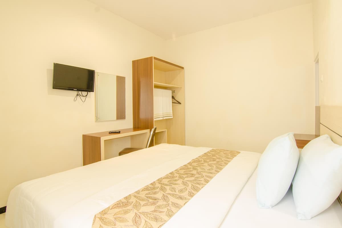 A hotel room with a bed, a TV mounted on the wall, a wooden desk, and a wardrobe.