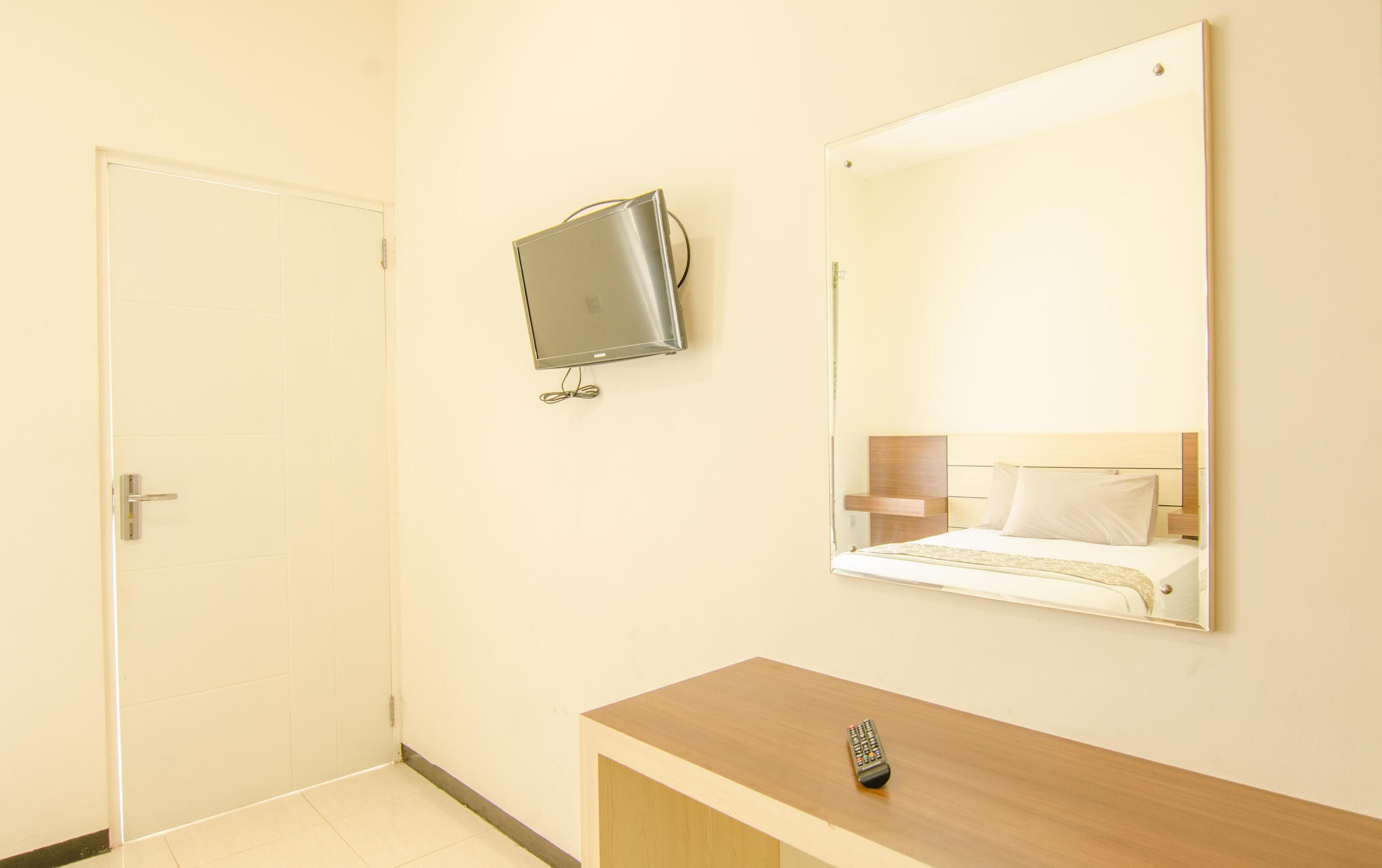 A hotel room with a wooden vanity, a bed with white linens, a television mounted on the wall, and a door.