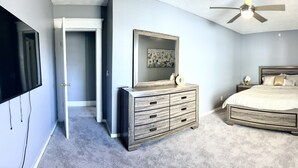 Un dormitorio con cama, cómoda, espejo, ventilador de techo y televisor.