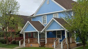 Una casa residencial de dos pisos con fachada azul, un porche delantero y un camino de entrada visible.