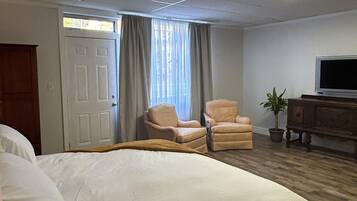 A hotel room with a large bed, two armchairs, a television, and a potted plant.