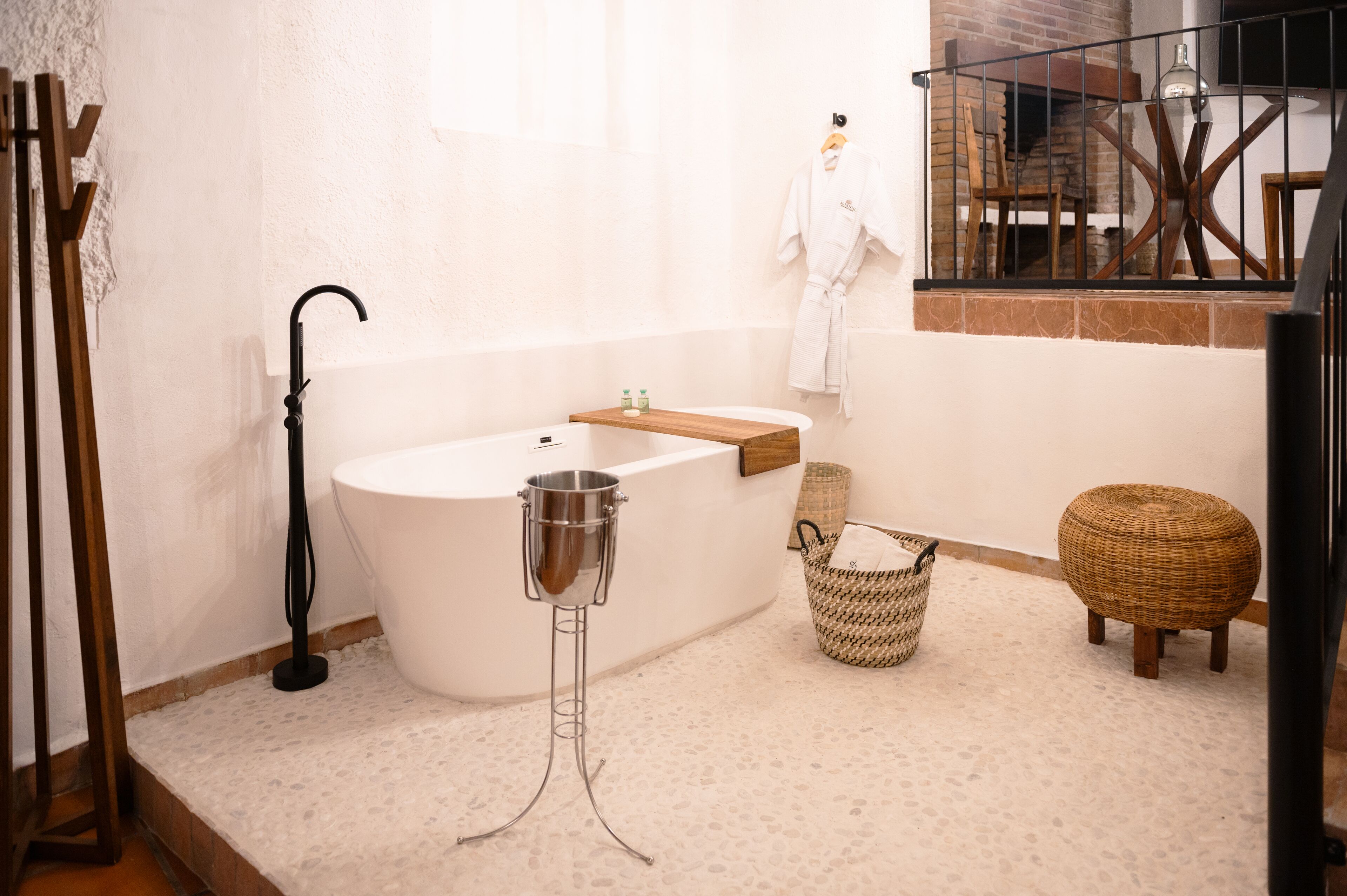 A modern bathroom with a freestanding bathtub, a wooden vanity, a wicker basket, and a round wicker stool.