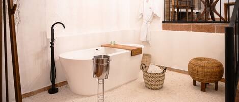 A modern bathroom with a freestanding bathtub, a wooden vanity, a wicker basket, and a round wicker stool.