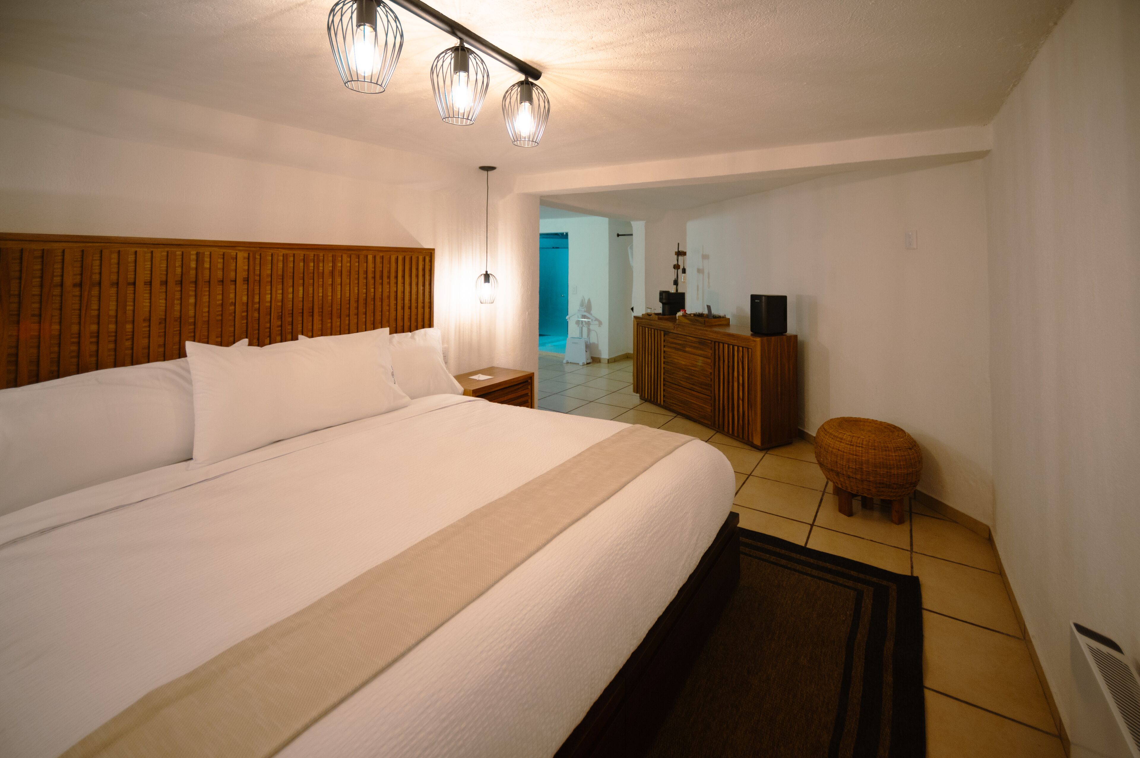 A bedroom with a large bed, wooden headboard, bedside tables, a dresser, a mirror, and a small stool.