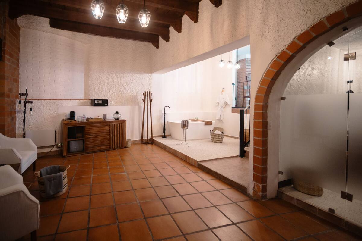 A spacious room with a tiled floor, a wooden bench, a white bathtub, and a brick archway.