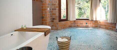A bathroom with a bathtub, a window with curtains, a tiled floor, and a wicker basket.