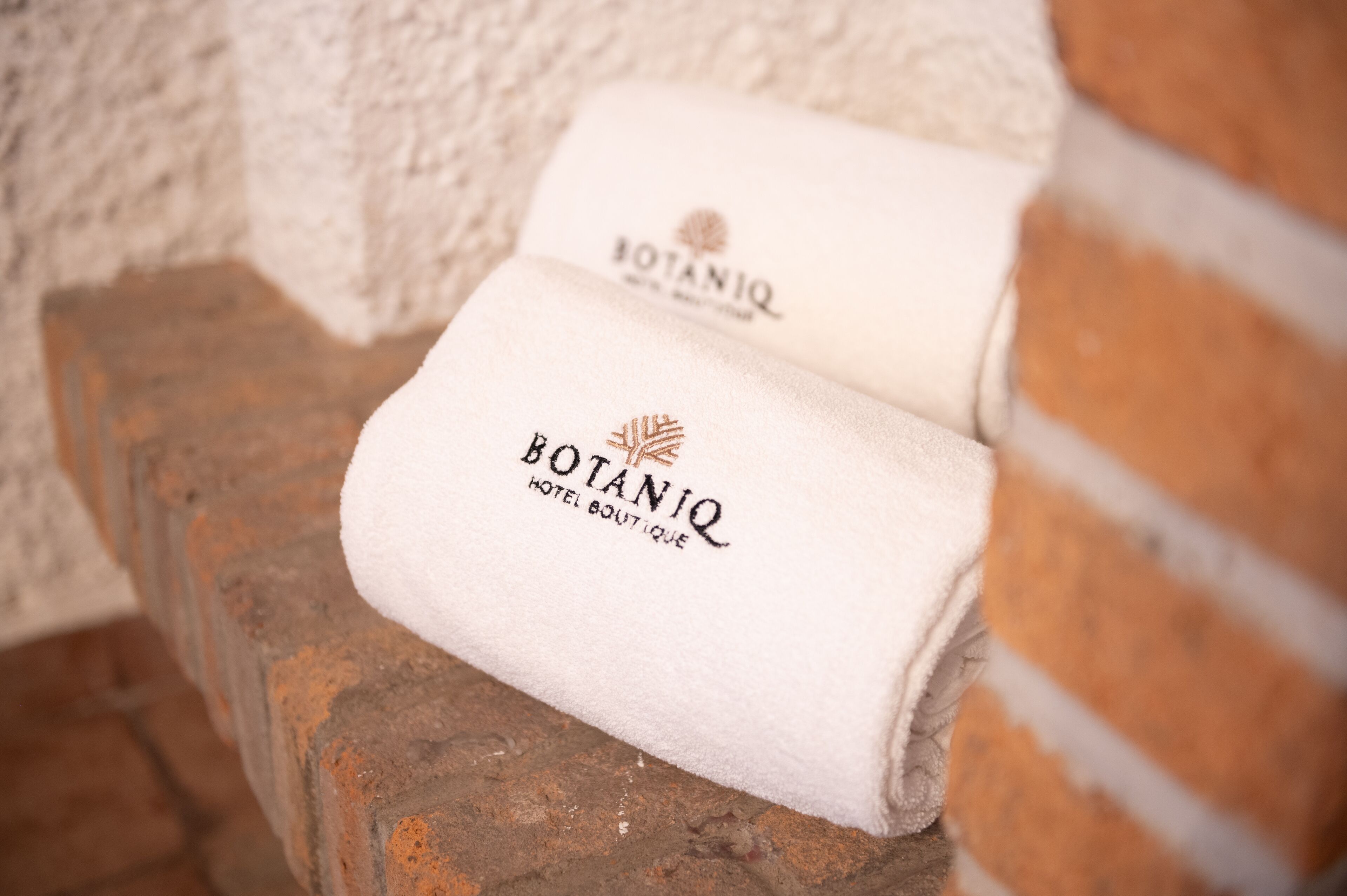 Dos toallas blancas con la inscripción 'BOTANIQ HOTEL BOUTIQUE', colocadas sobre un alféizar de ladrillo.