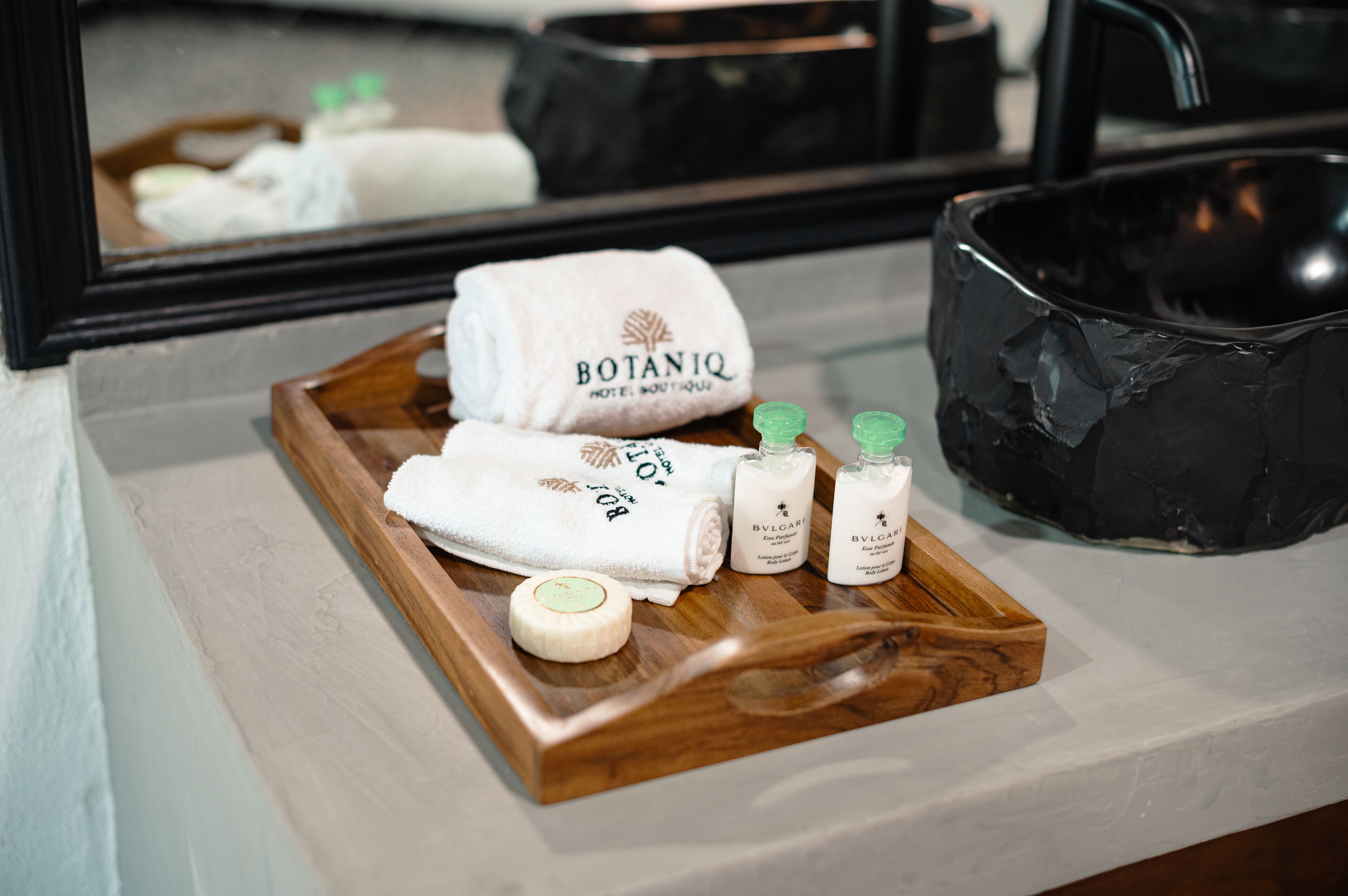 A wooden tray with a white towel, two bottles of skincare products, and a soap bar on a bathroom counter.