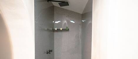 A modern shower area with a speckled floor, a ceiling-mounted showerhead, and a shelf with toiletries.
