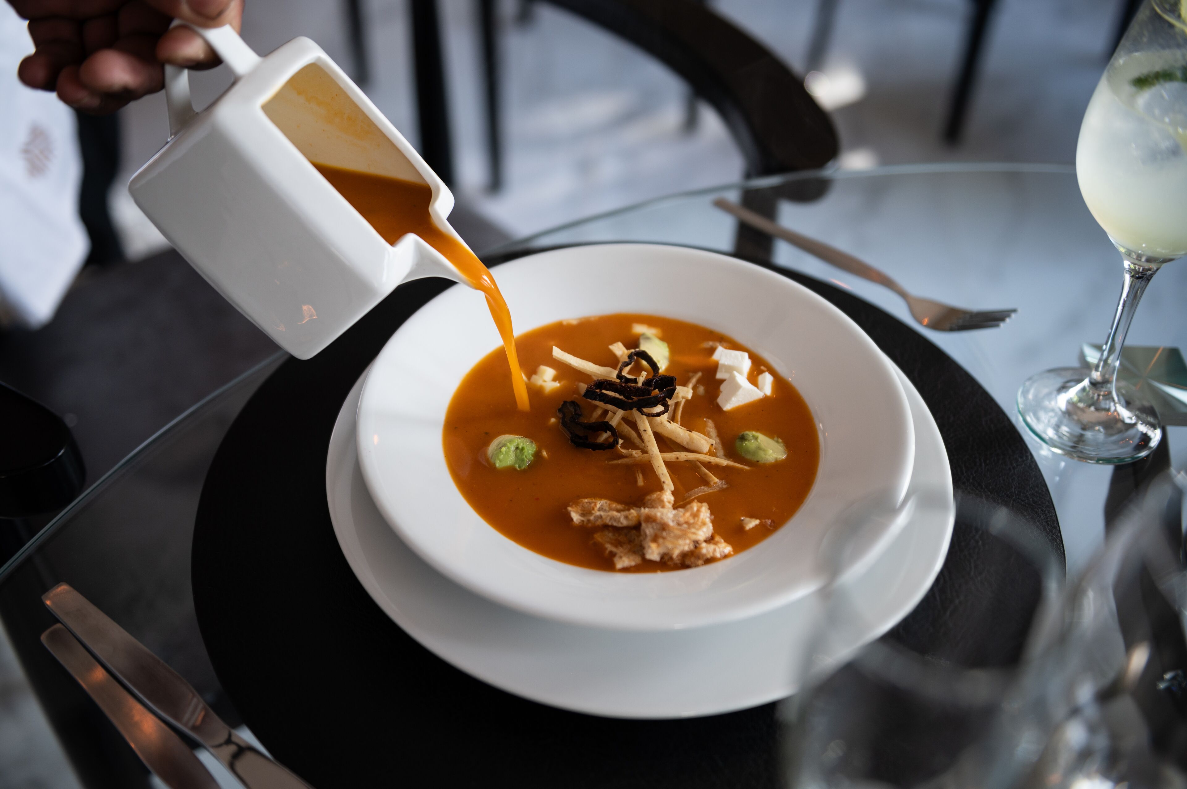 A bowl of soup with toppings being poured into it.