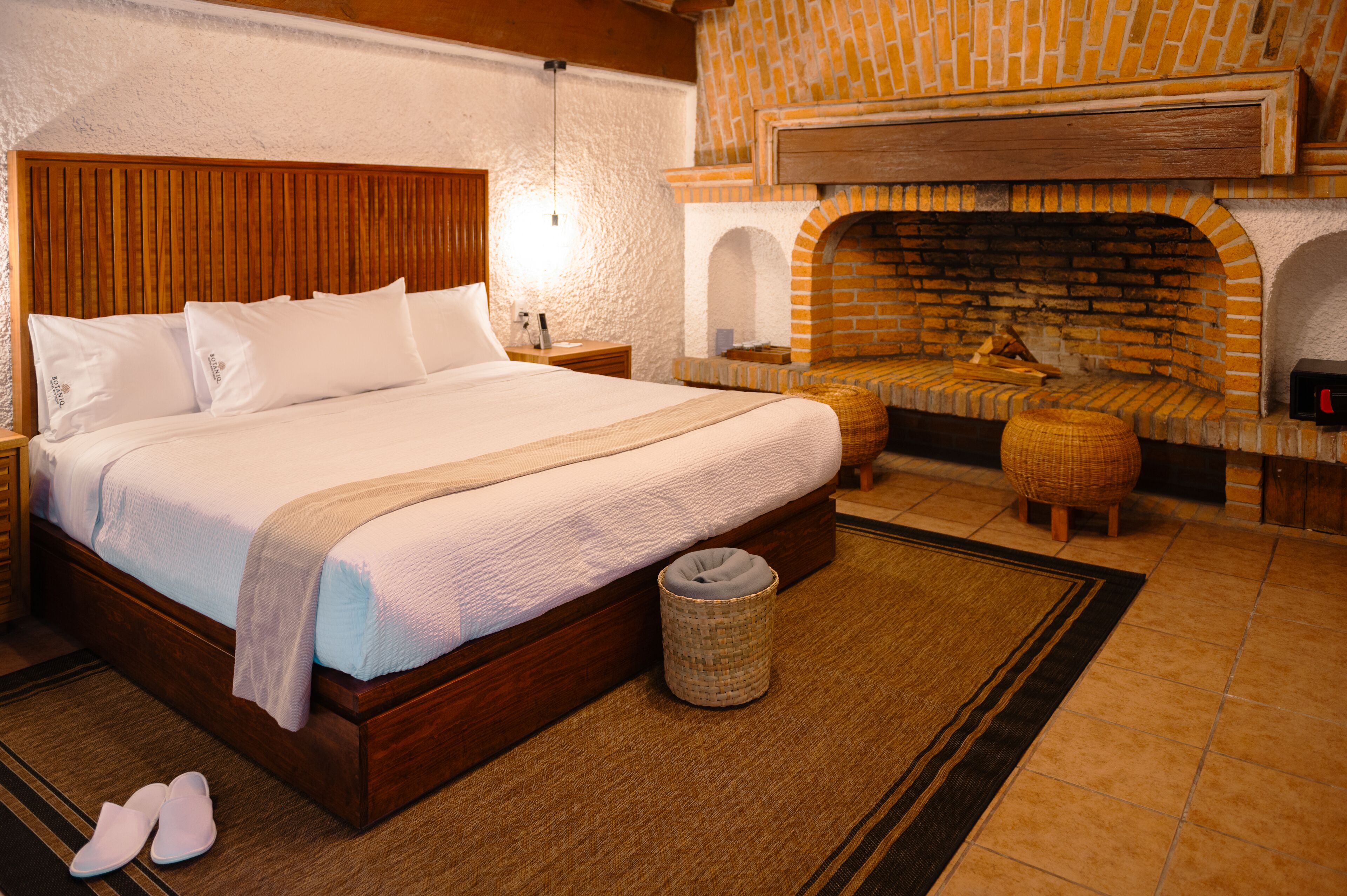 Una camera da letto con un letto in legno, un camino in mattoni e un poggiapiedi in vimini.