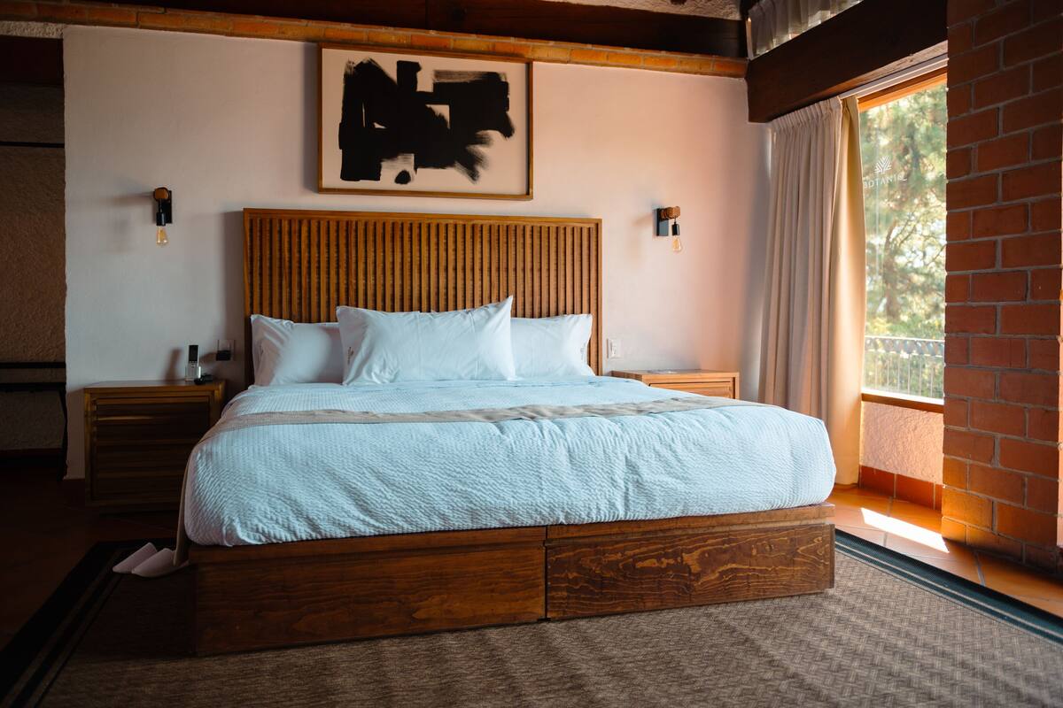 A neatly made bed with a wooden headboard, two bedside tables, and a large window with curtains.