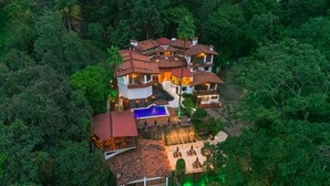 Una casa de varios pisos con piscina, rodeada de un bosque frondoso.