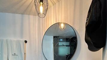 A bathroom with a black sink, a round mirror, a towel rack, and a wooden tray with toiletries.