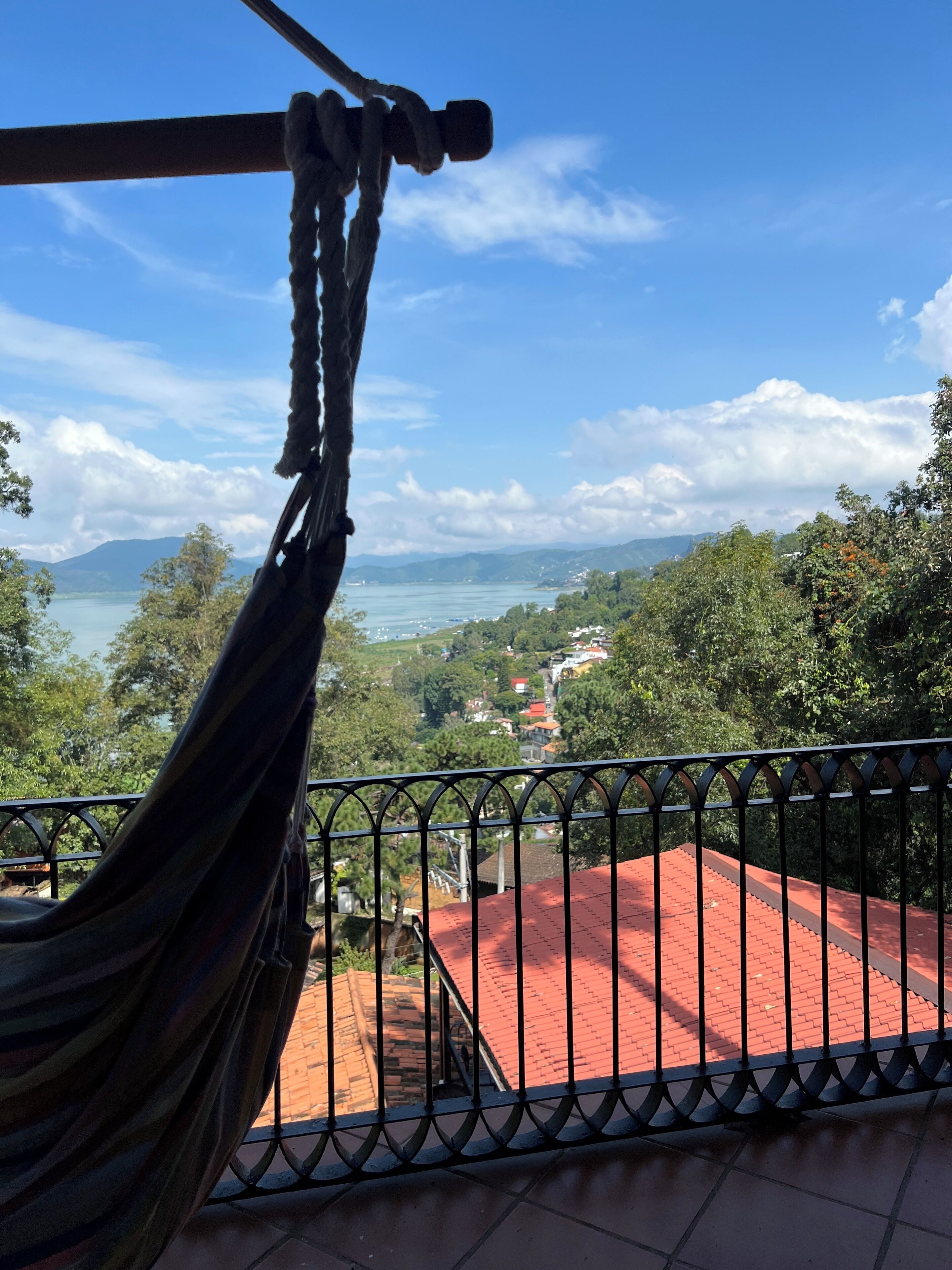A hammock on a balcony overlooking a scenic view of a lake, trees, and distant mountains.