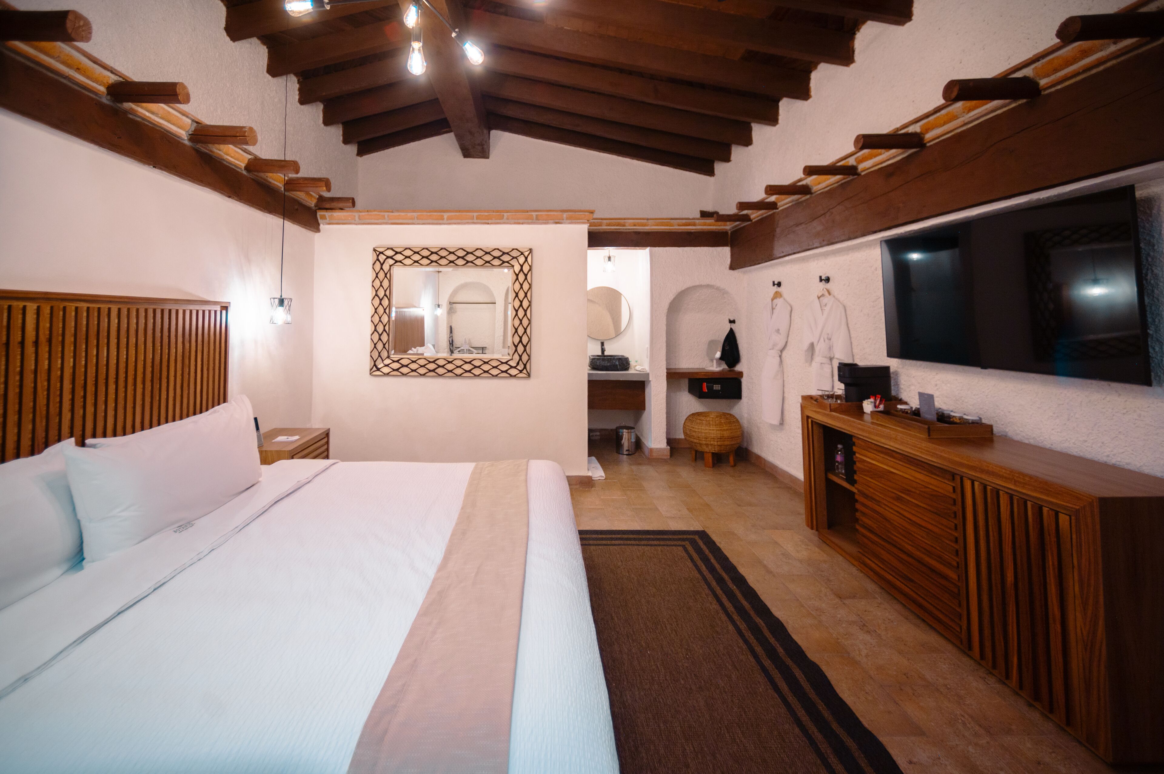 A bedroom with a large bed, wooden headboard, a mirror, a television, and a wooden cabinet.