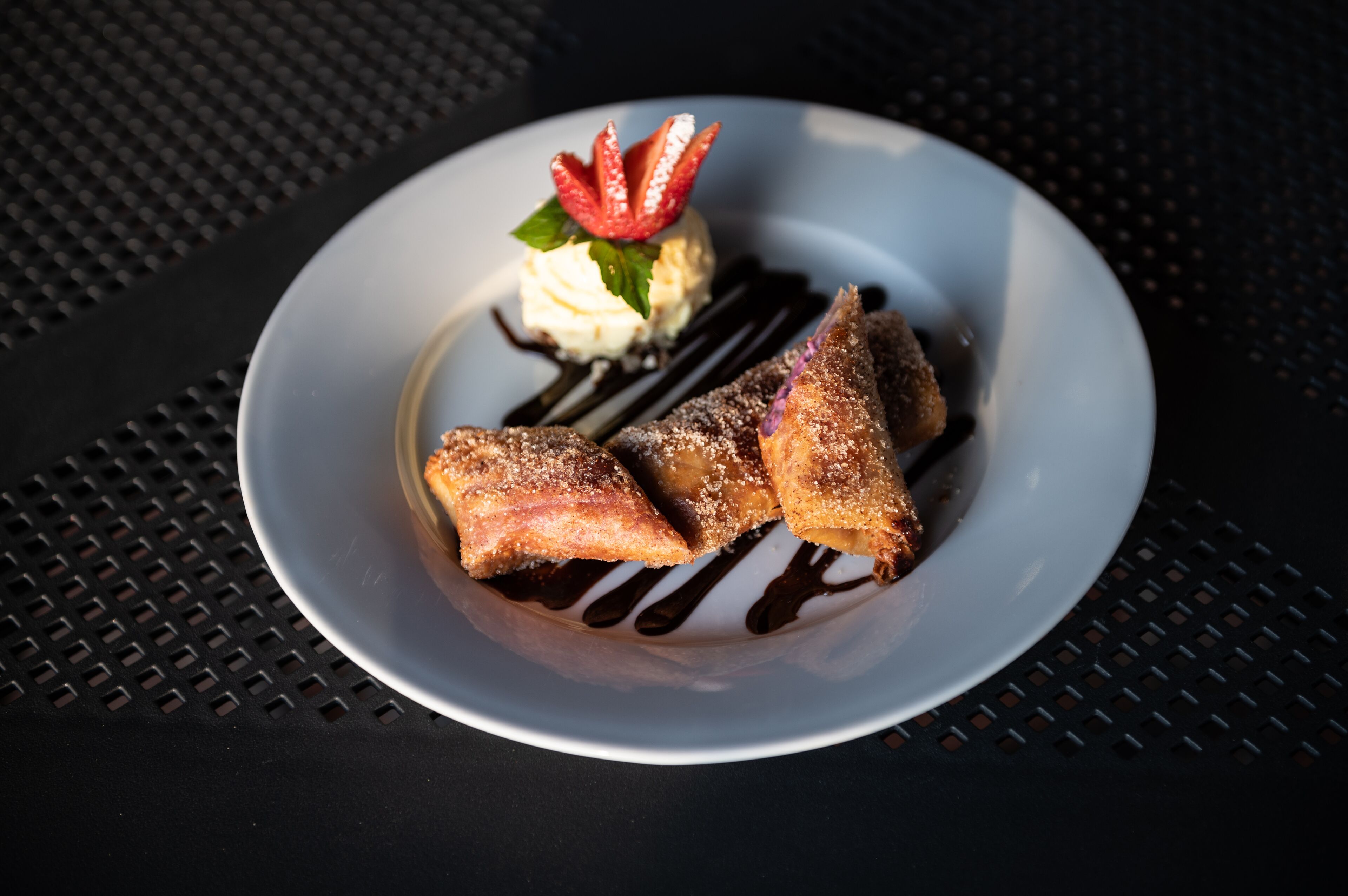 A plate with a dessert consisting of a triangular pastry, a scoop of ice cream, and a strawberry garnish.