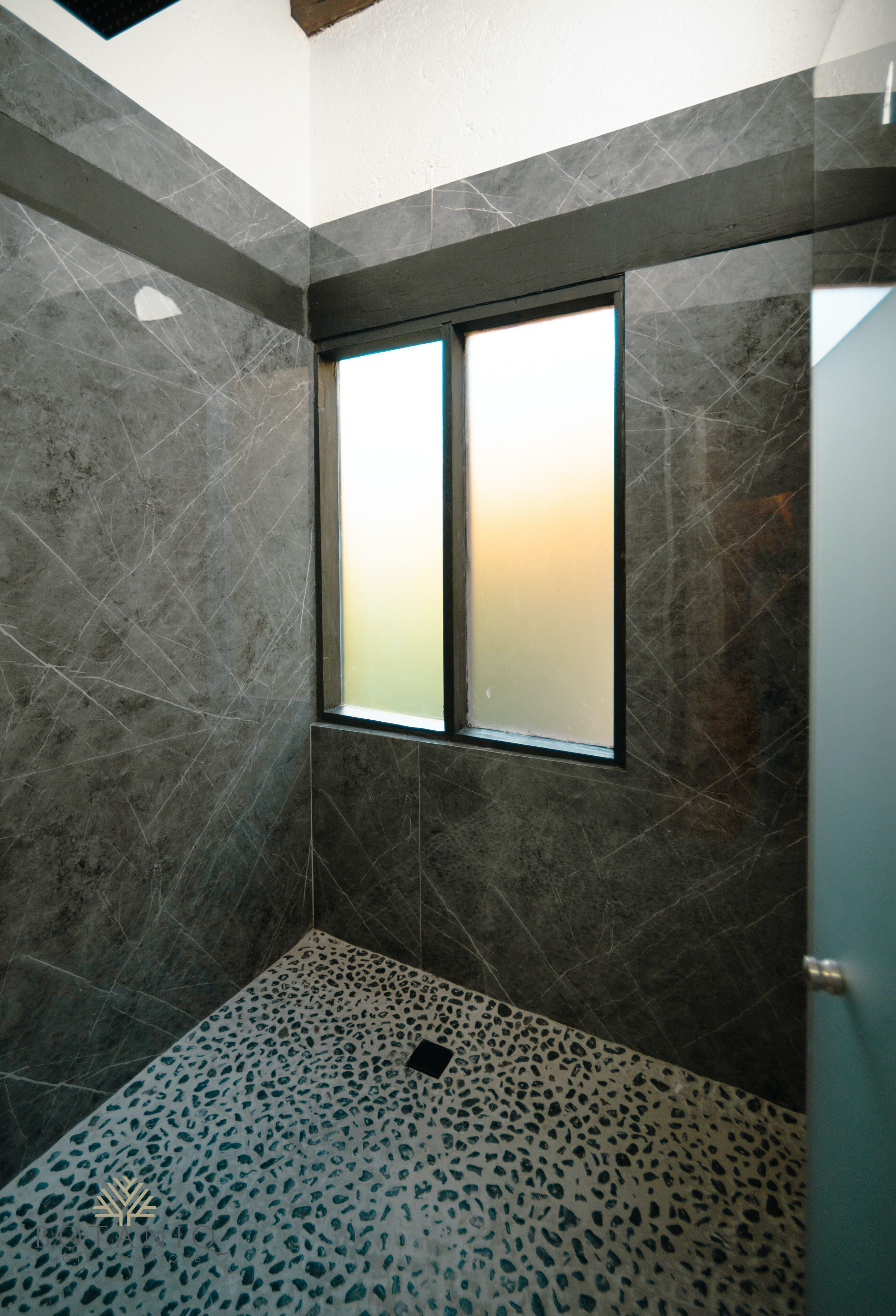 A bathroom with a large window, dark marble walls, and a speckled floor.