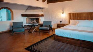 A bedroom with a bed, two chairs, a small table, a fireplace, and a nightstand.