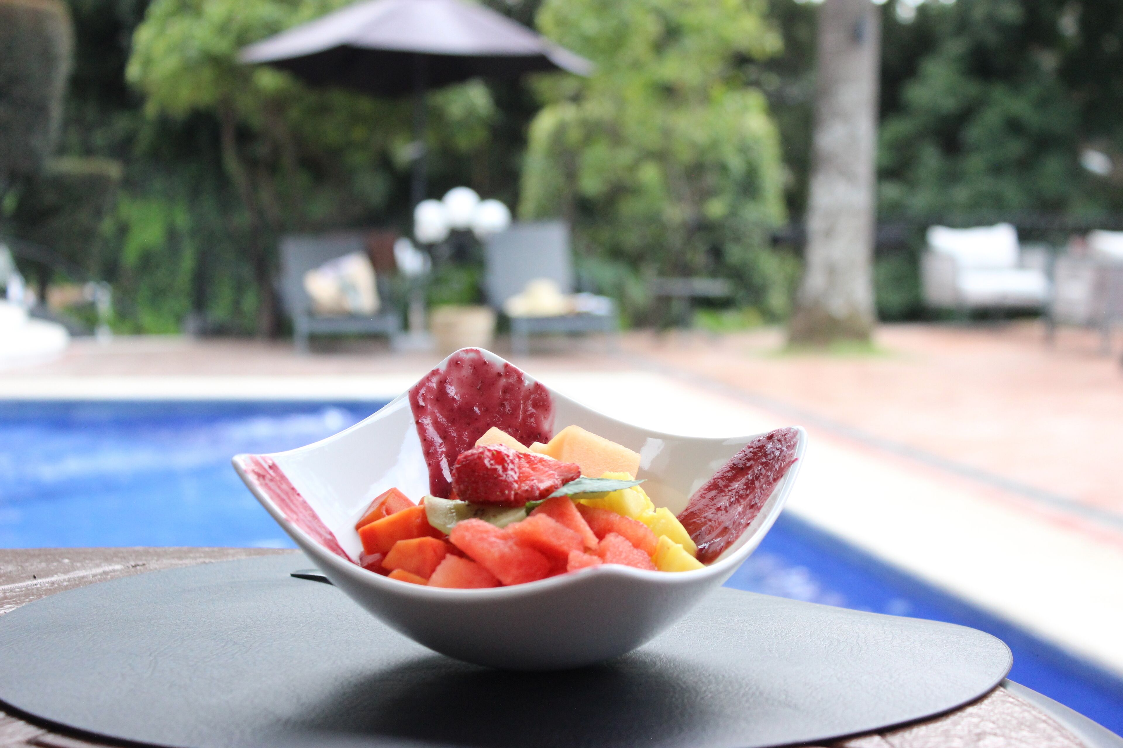 A bowl of fruit on a table near a pool.