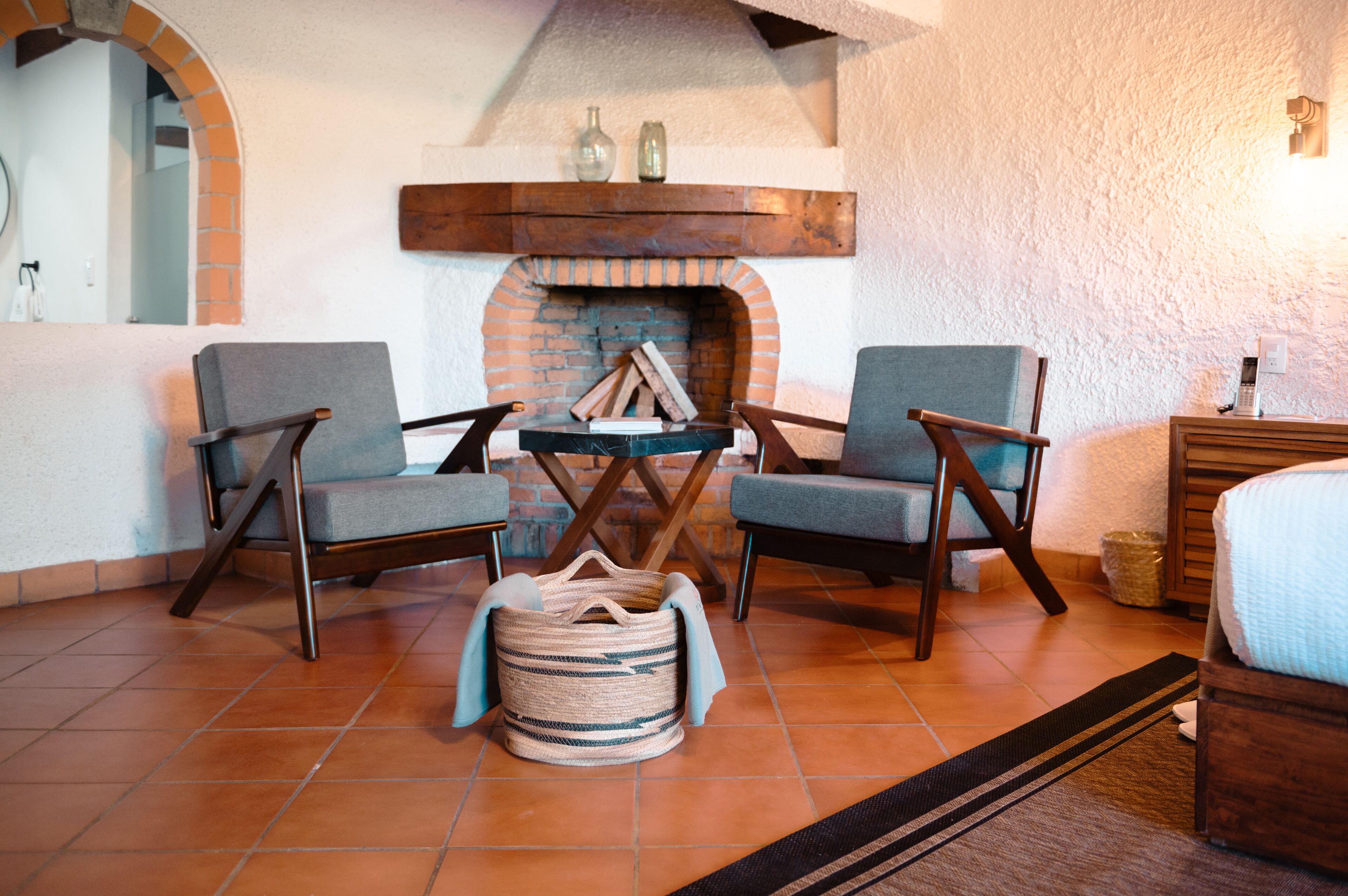 A cozy room with a brick fireplace, two armchairs, a small table, and a wicker basket.