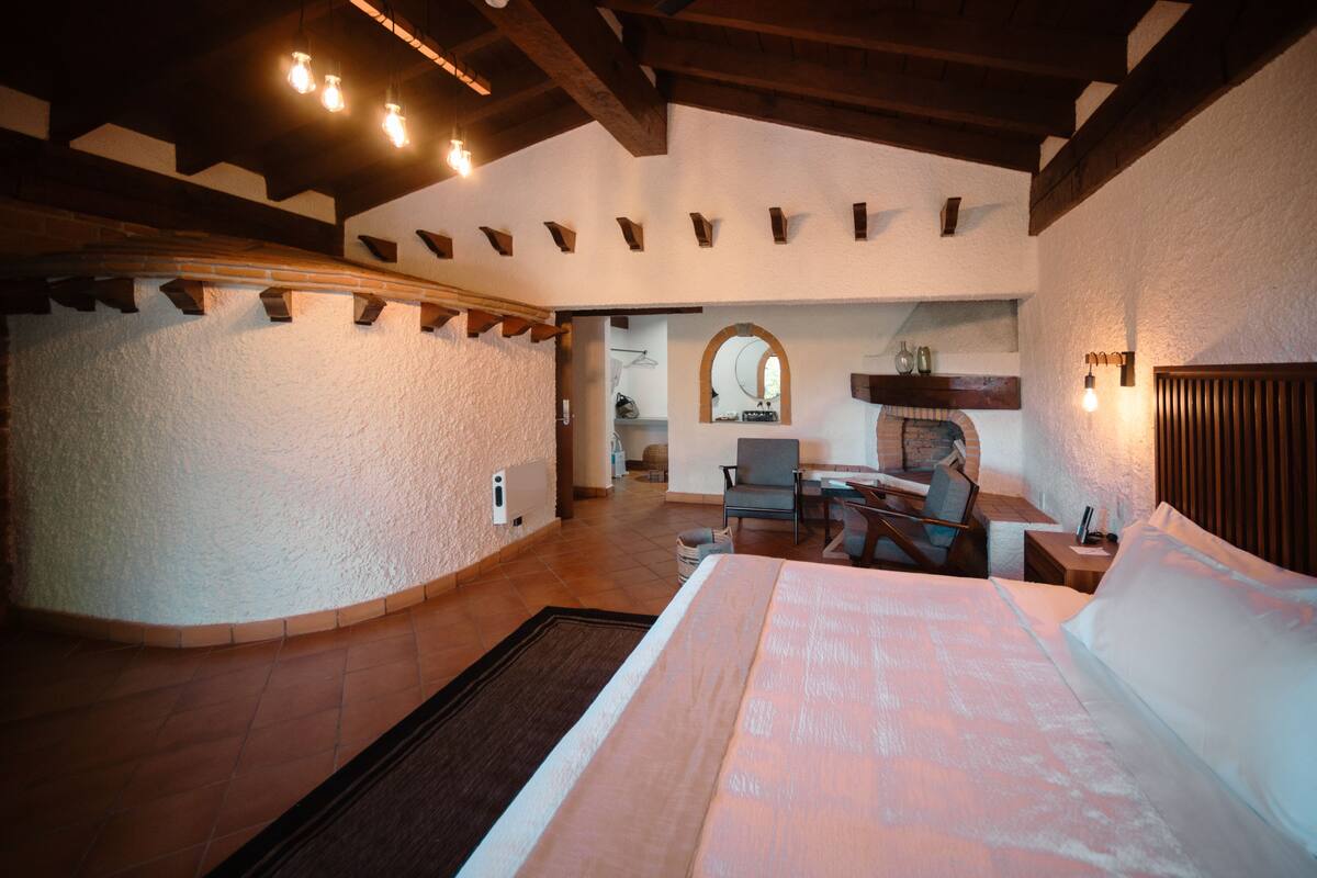 A spacious bedroom with a large bed, a wooden headboard, and a built-in fireplace.