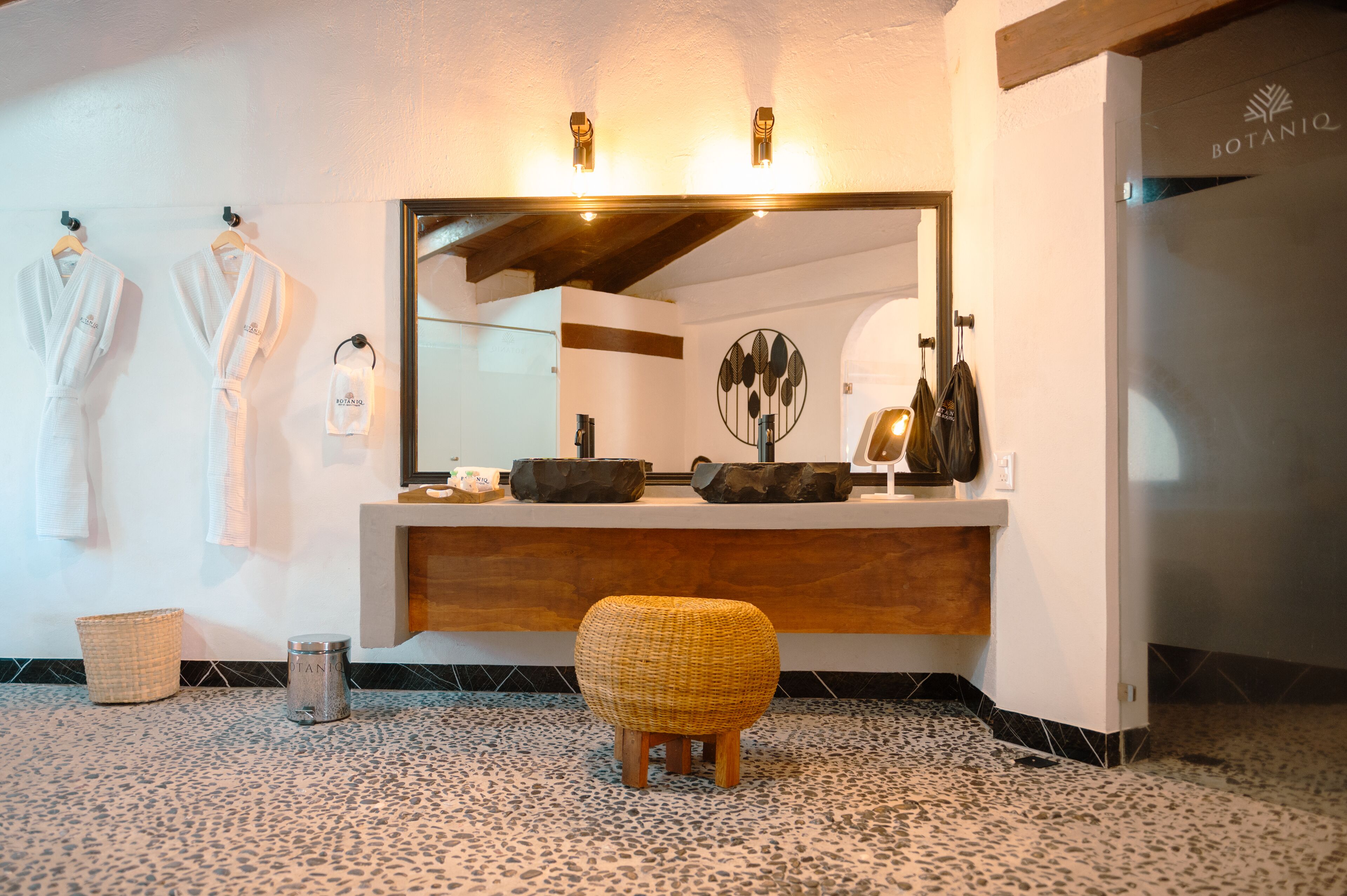 A bathroom with a large mirror, wooden counter, and a woven stool.