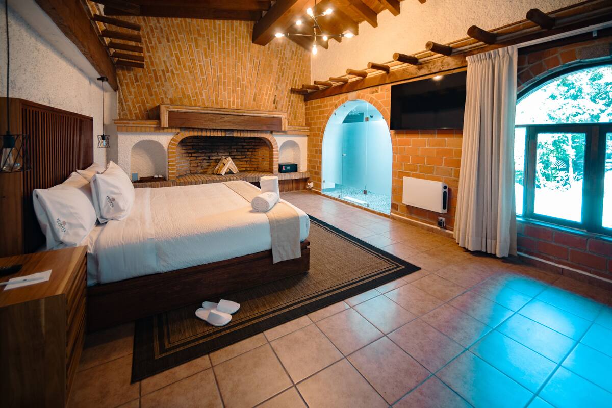 A spacious bedroom with a large bed, a fireplace, and a view of the outdoors.