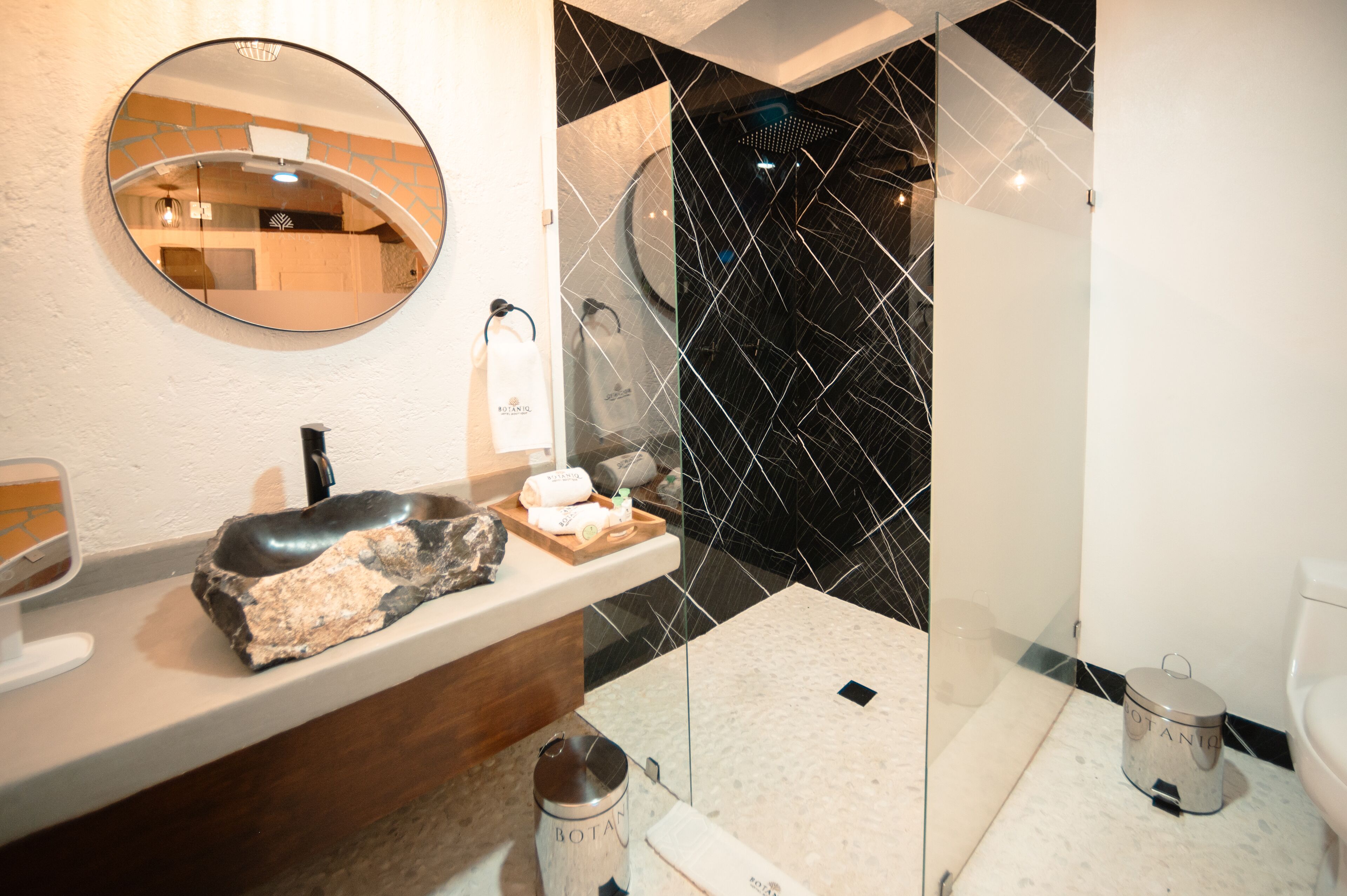 A modern bathroom with a marble sink, a round mirror, a black and white tiled shower, and a toilet.
