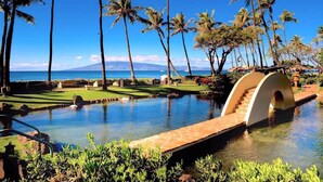 Ein Resort-Pool mit Brücke, Palmen und Blick auf den Ozean.