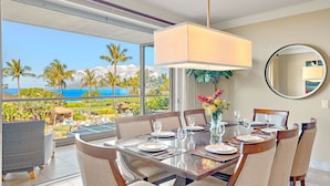 A dining area with a glass table, chairs, and a view of the ocean.