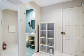 A room with a white door, a white shelf unit with books, and a blue wall with a mirror and a round mirror.