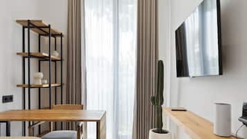 A modern living room with a wooden desk, a mounted TV, a cactus plant, and a ceiling fan.