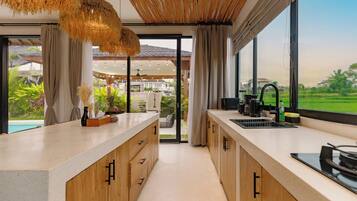 A modern kitchen with a large island, wooden cabinets, and a view of a lush garden and pool.