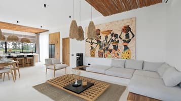 A modern living room with a large sofa, a coffee table, and a dining area with chairs and a table.