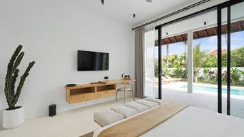 Quarto moderno com uma cama grande, TV na parede, mesa de console de madeira e vista para uma piscina e vegetação lá fora.