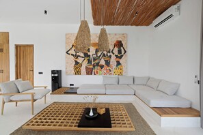 A modern living room with a sectional sofa, a coffee table, and a large abstract painting. - Marbella Villa by DH (Ubud)