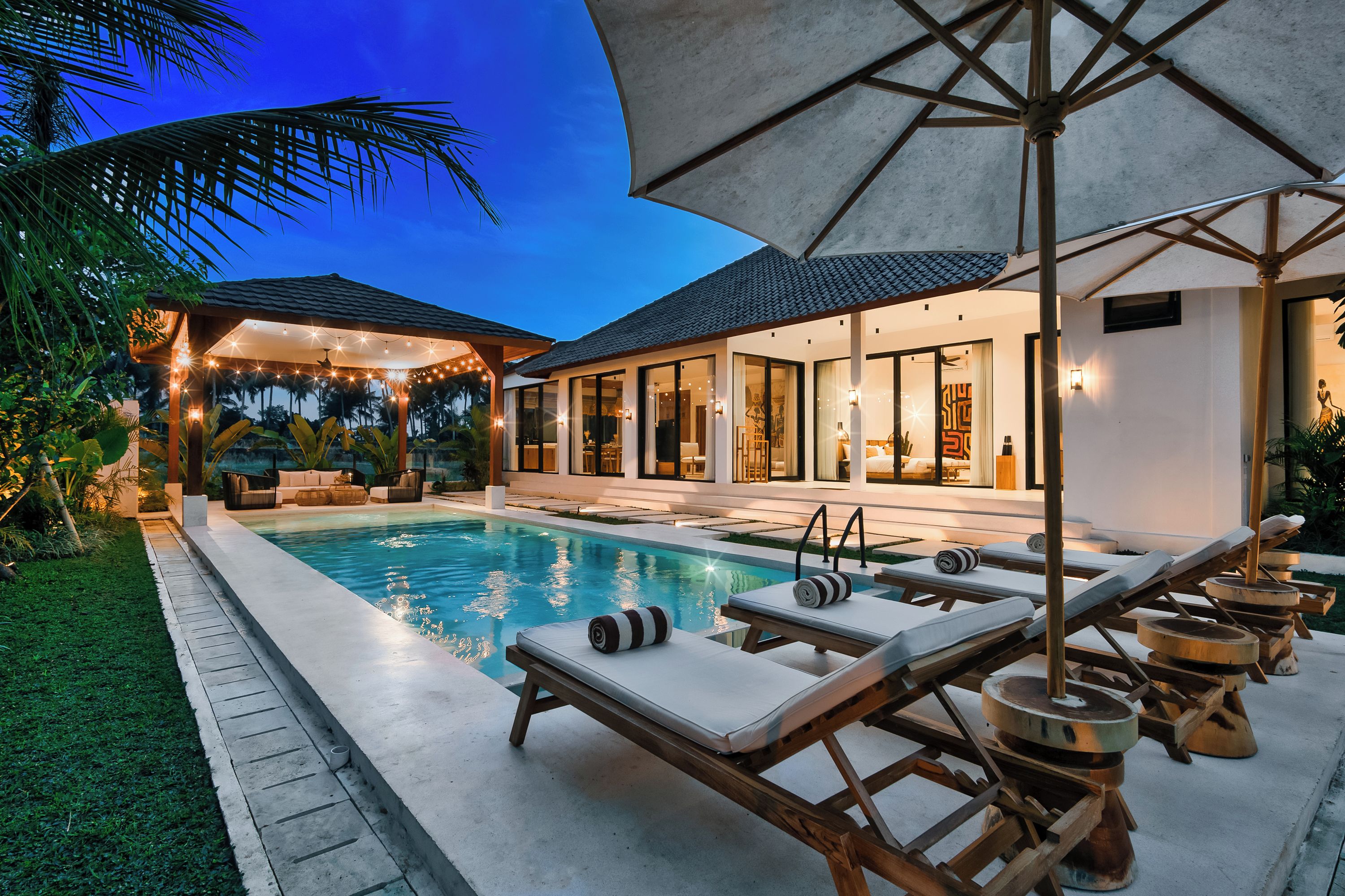 A modern poolside area with lounge chairs, a swimming pool, and a covered seating area with string lights.