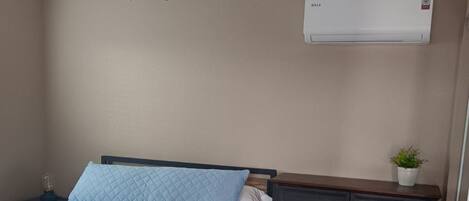 A bedroom with a bed, a ceiling fan, a dresser, and an air conditioning unit.