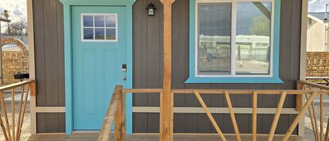 A small, two-story building with a wooden deck and a turquoise door.