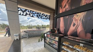 Un épicerie avec des chariots, un présentoir réfrigéré contenant divers produits alimentaires et une grande affiche sur le mur.