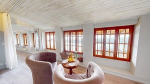 Una habitación amplia con techos altos y ventanas grandes, que cuenta con una zona de estar confortable y una mesa dispuesta para comer.