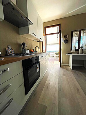 Uma cozinha moderna com fogão, forno e armários. Há uma janela com cortinas e vista para o exterior.