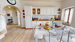 Una cucina moderna con mobili bianchi, un'area pranzo con un tavolo in marmo e una sveglia appesa al muro.