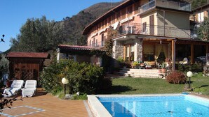 Una casa de dos pisos con piscina, rodeada de vegetación y con una montaña de fondo.