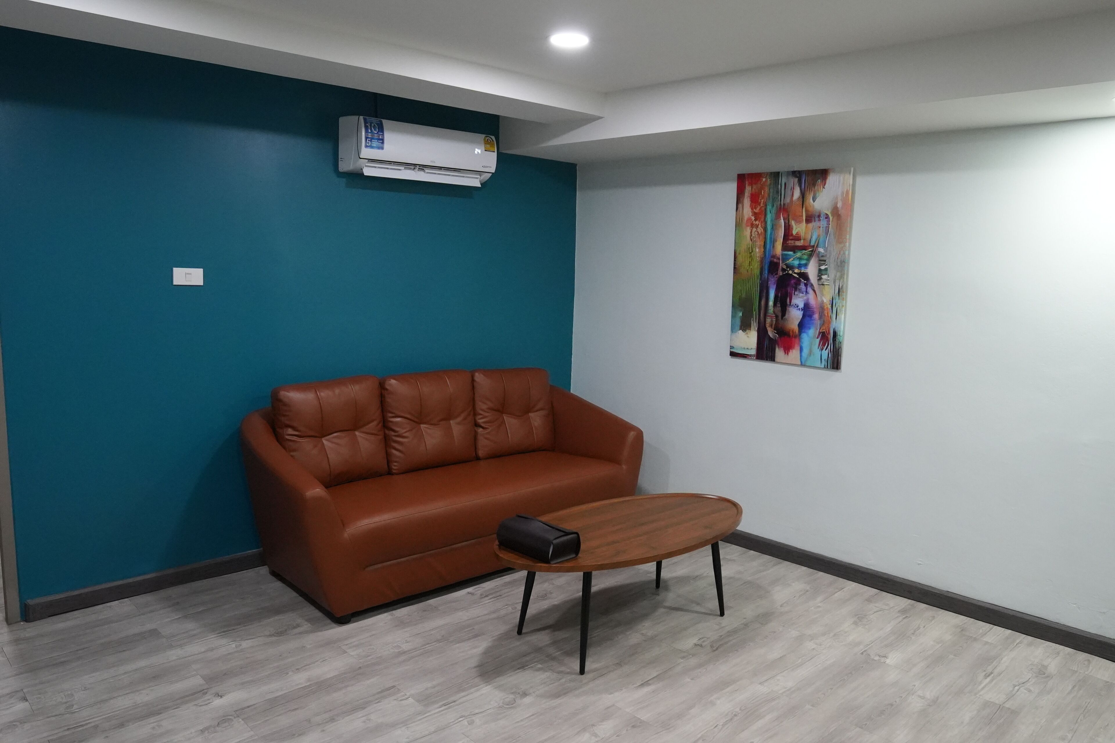 A room with a brown leather sofa, a wooden coffee table, teal walls, and a colorful abstract painting.